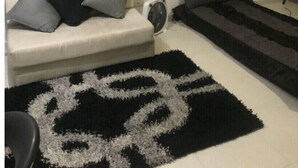 Uma sala de estar com um sofá, um tapete preto e branco e duas pinturas grandes na parede.