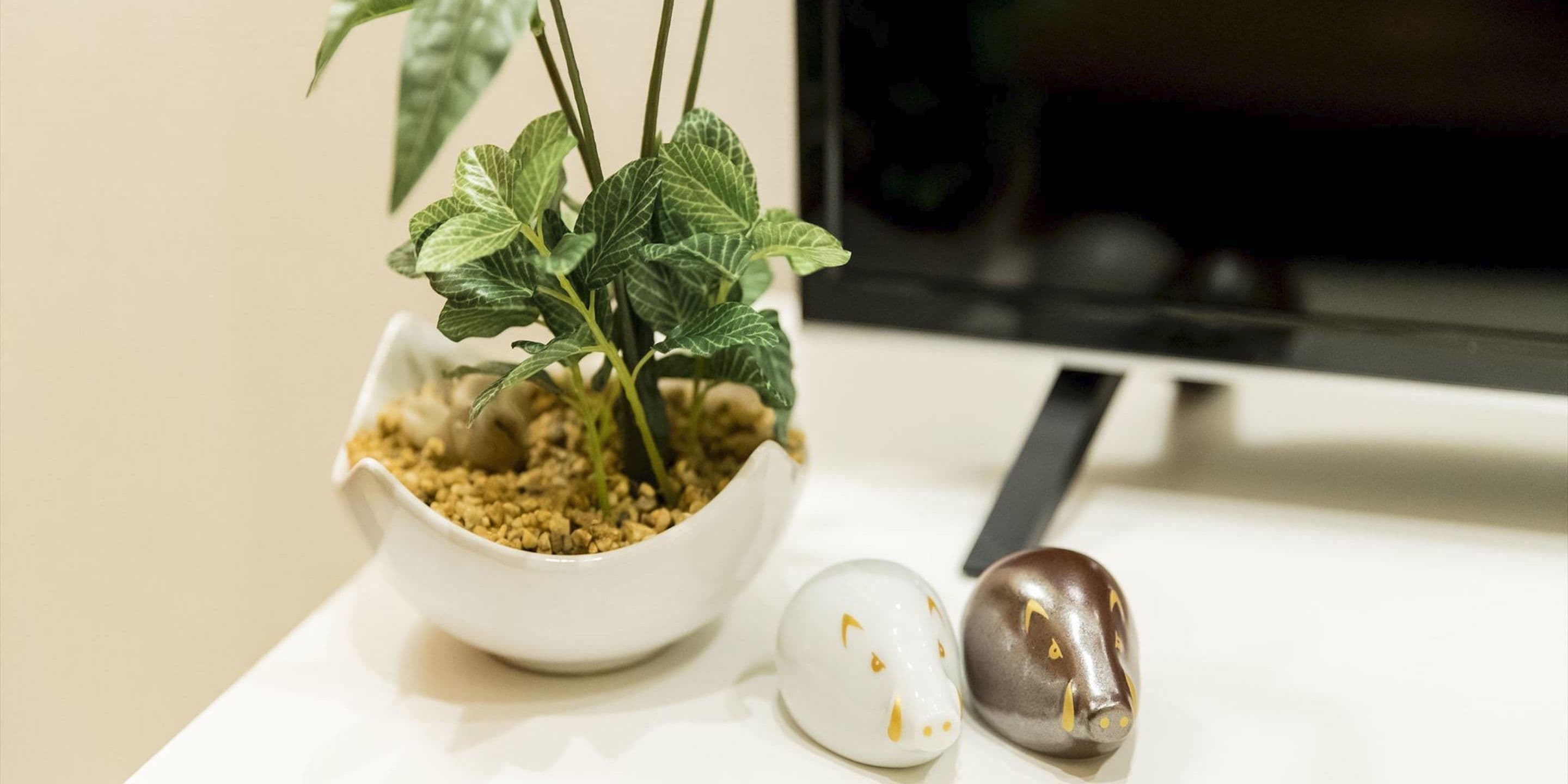 A white bowl with a plant and two ceramic animal figurines on a white surface.
