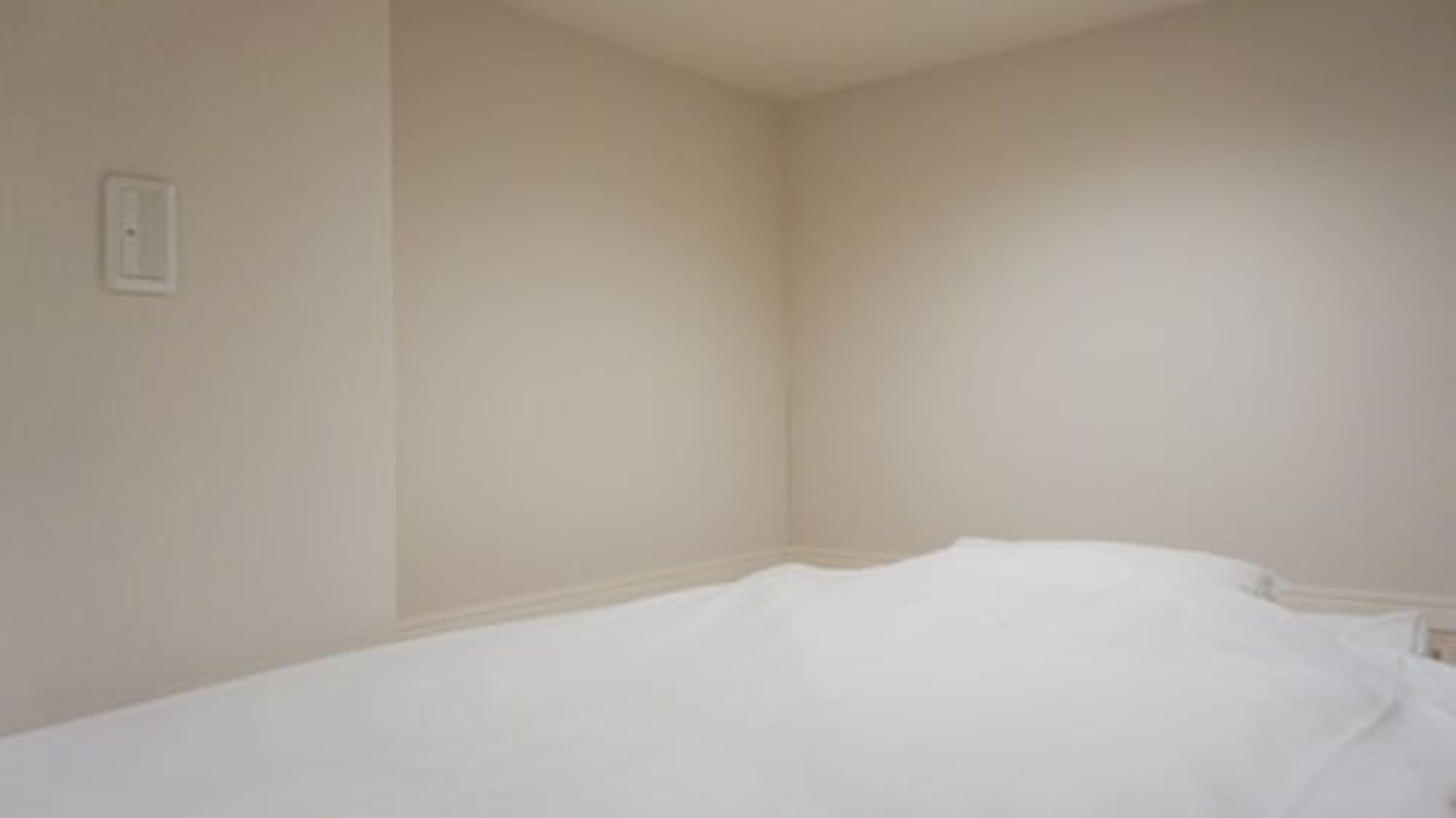 Une petite pièce vide, avec un lit simple et un interrupteur sur le mur.