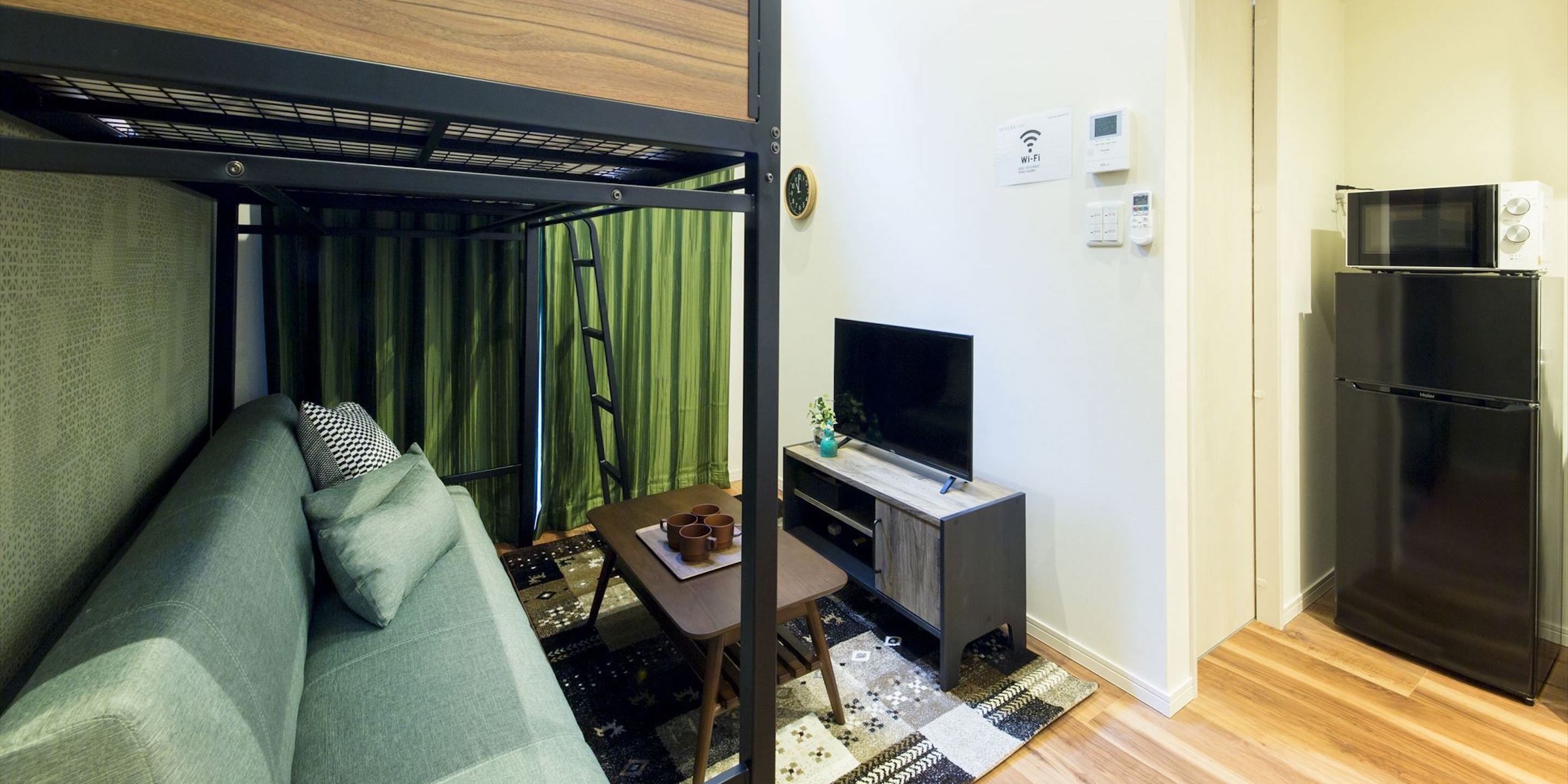 Un espace de vie compact comprenant un canapé, un téléviseur posé sur un meuble, un réfrigérateur et un four à micro-ondes placé sur le dessus du réfrigérateur.