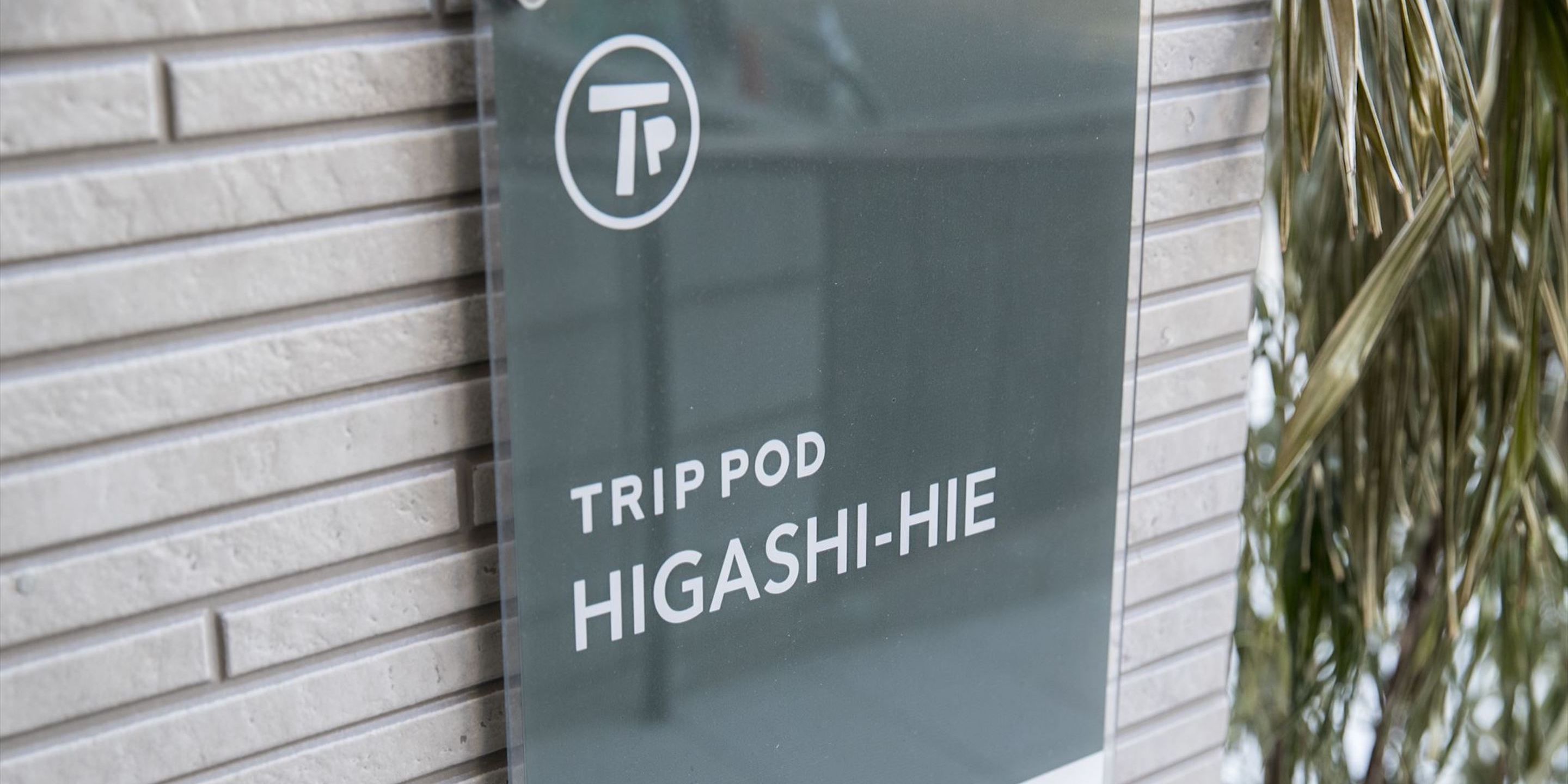 A sign with the text "TRIP POD HIGASHI-HIE" on a brick wall.