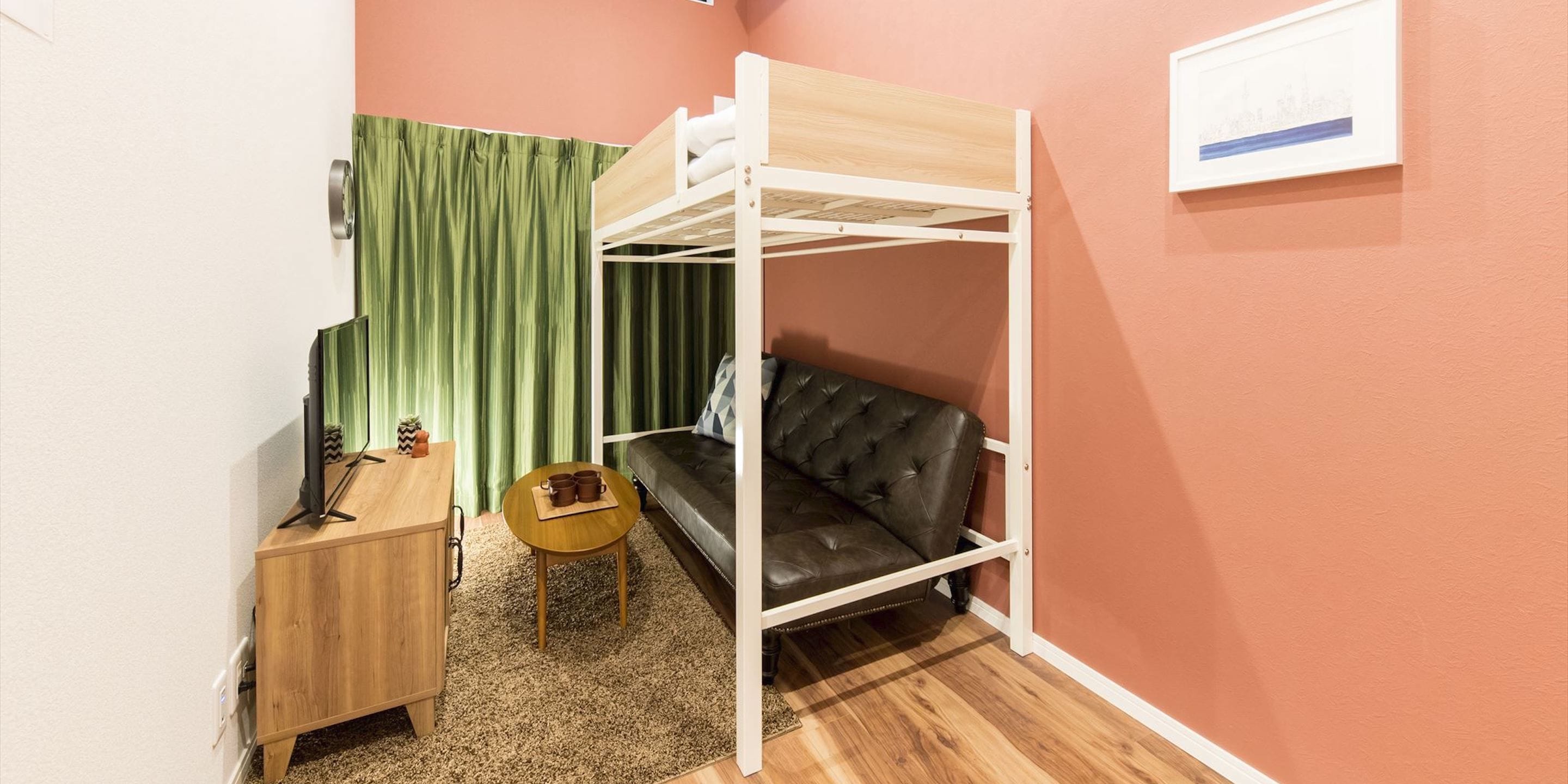 A bunk bed with a wooden frame, a leather sofa, a small wooden table with cups, a green curtain, and a framed picture on the wall.