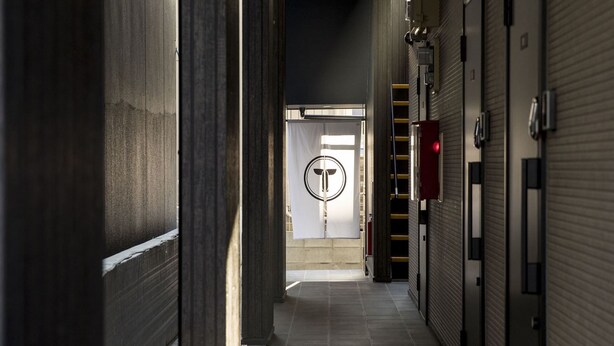 A corridor with closed shuttered doors, a fire exit sign, and a fire extinguisher on the wall. - Trip Pod Higashihie (Fukuoka)
