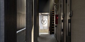 A corridor with closed shuttered doors, a fire exit sign, and a fire extinguisher on the wall. - Trip Pod Higashihie (Fukuoka)