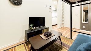 A modern living room with a flat-screen TV, a coffee table with mugs, a blue sofa, and a wooden floor. - Trip Pod Higashihie (Fukuoka)