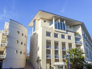Un bâtiment moderne abritant un restaurant et une pizzeria au rez-de-chaussée, doté de balcons et offrant une vue sur un ciel dégagé.