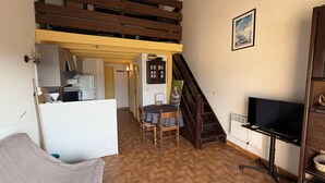 Un espacio habitable compacto con cama elevada, comedor, cocina y televisión.