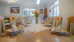 A dining room with a wooden table set for a meal, chairs, and a vase of flowers. - ***** Luisenlund Apartment, 5 bedrooms, 3 bathrooms, made-up beds, Wi-Fi, prime location, wood-burning stove, sauna (Ostseebad Prerow)