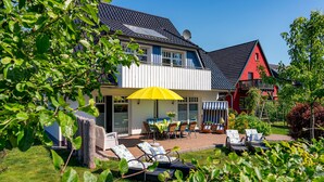 A two-story house with a covered patio, outdoor seating, and a red barn in the background. - ***** Luisenlund Apartment, 5 bedrooms, 3 bathrooms, made-up beds, Wi-Fi, prime location, wood-burning stove, sauna (Ostseebad Prerow)