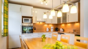 A modern kitchen with white cabinets, a microwave, oven, and a dining area with a table set for four. - ***** Luisenlund Apartment, 5 bedrooms, 3 bathrooms, made-up beds, Wi-Fi, prime location, wood-burning stove, sauna (Ostseebad Prerow)