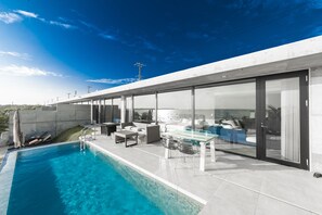 A modern outdoor pool area with a glass table and chairs, a lounge chair, and a view of the sea. - D's GROW RESORT Infinity Pool Villa (Miyakojima)