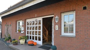 A brick building with a white door, a window, and a small porch area with potted plants and a pumpkin. - Single standing top equipped house for up to 14 people. (Battenberg/Dodenau (Eder))