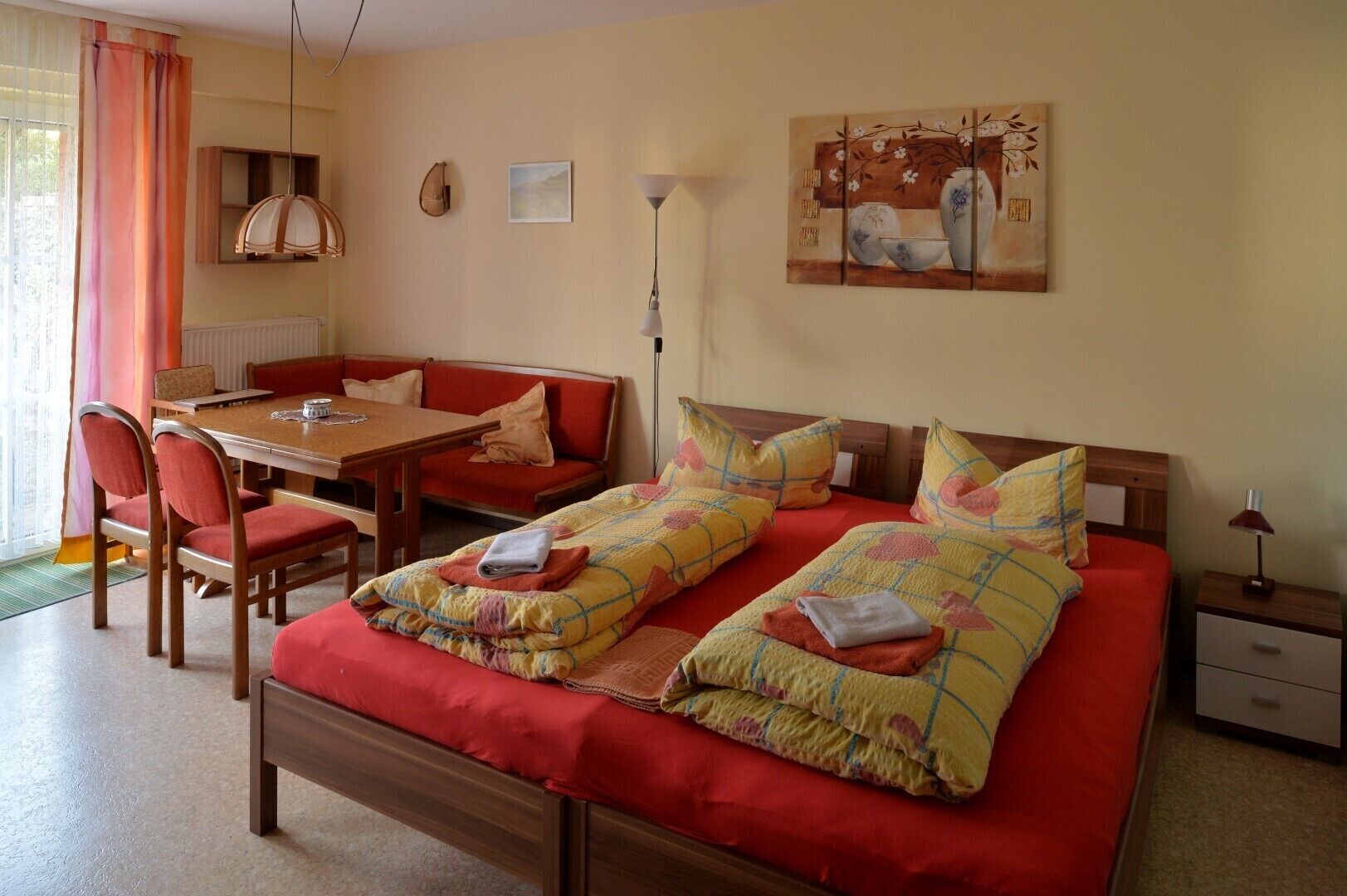 A hotel room with a large bed, a dining table, chairs, a sofa, a lamp, and artwork on the wall.