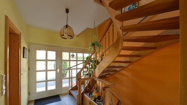 A wooden staircase with a handrail, a hanging light fixture, and a door with multiple windows. - Single standing top equipped house for up to 14 people. (Battenberg/Dodenau (Eder))