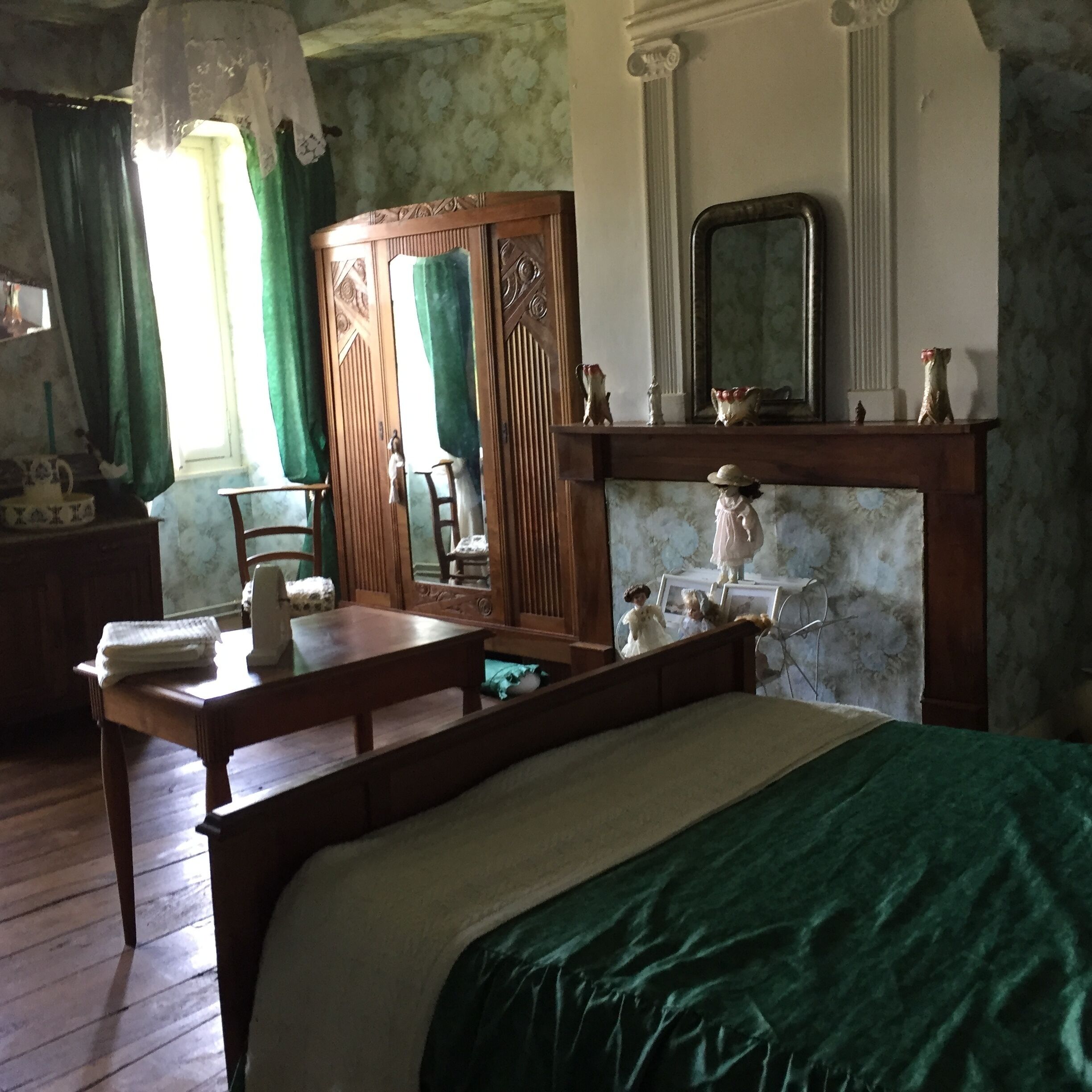 Quarto com cama, cómoda de madeira, espelho e lareira com figuras decorativas.
