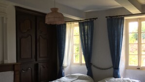 Una habitación con dos camas individuales, un armario de madera, una lámpara colgante y una ventana con cortinas azules.