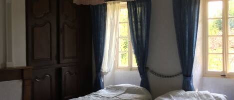 A room with two single beds, a wooden wardrobe, a hanging light fixture, and a window with blue curtains.