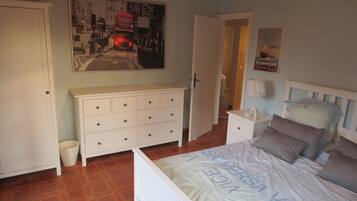 A bedroom with a bed, a dresser, a nightstand, a poster on the wall, and a door leading to another room.