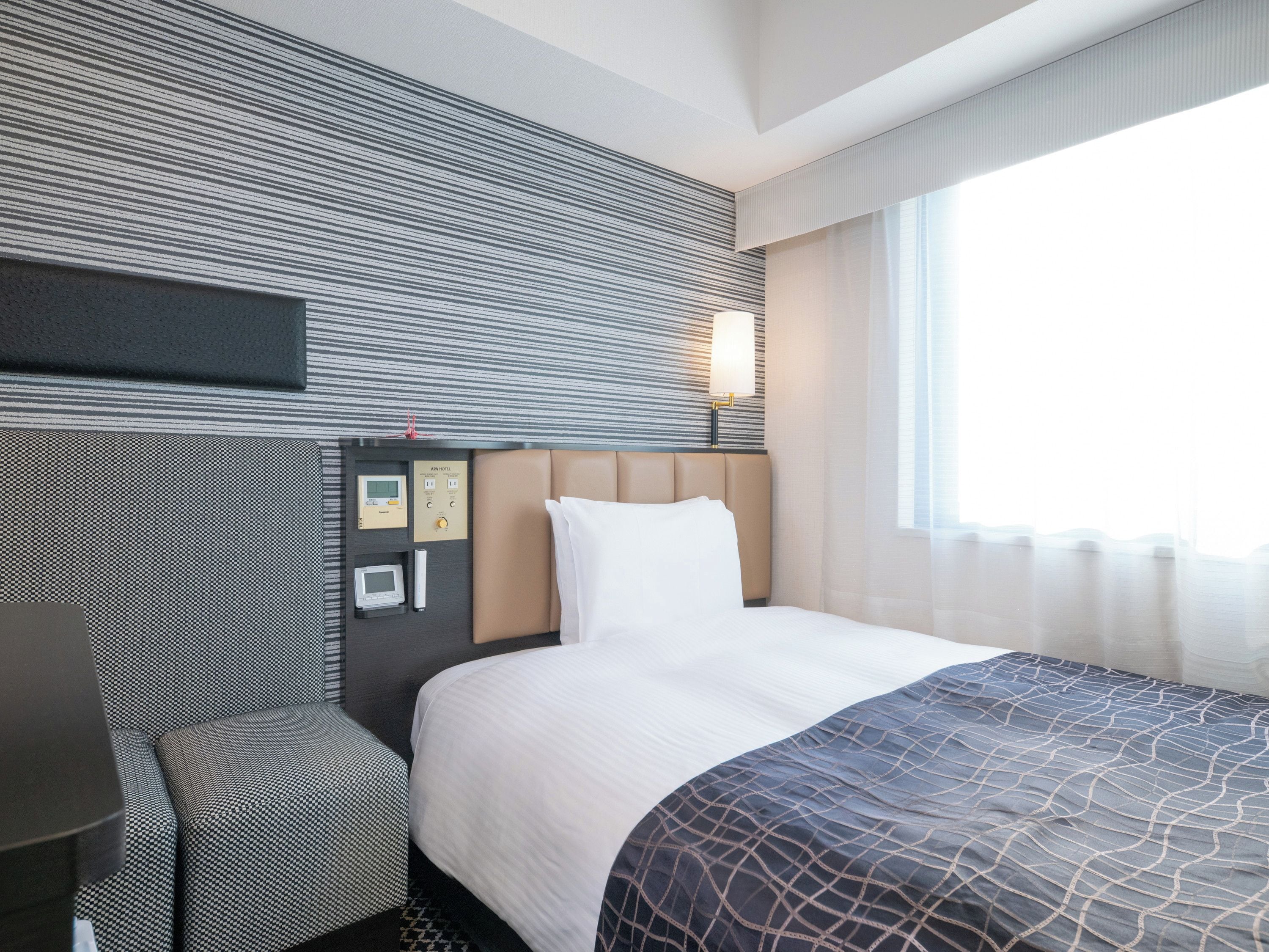 A hotel room with a bed, a bedside table, a control panel, and a window with curtains.