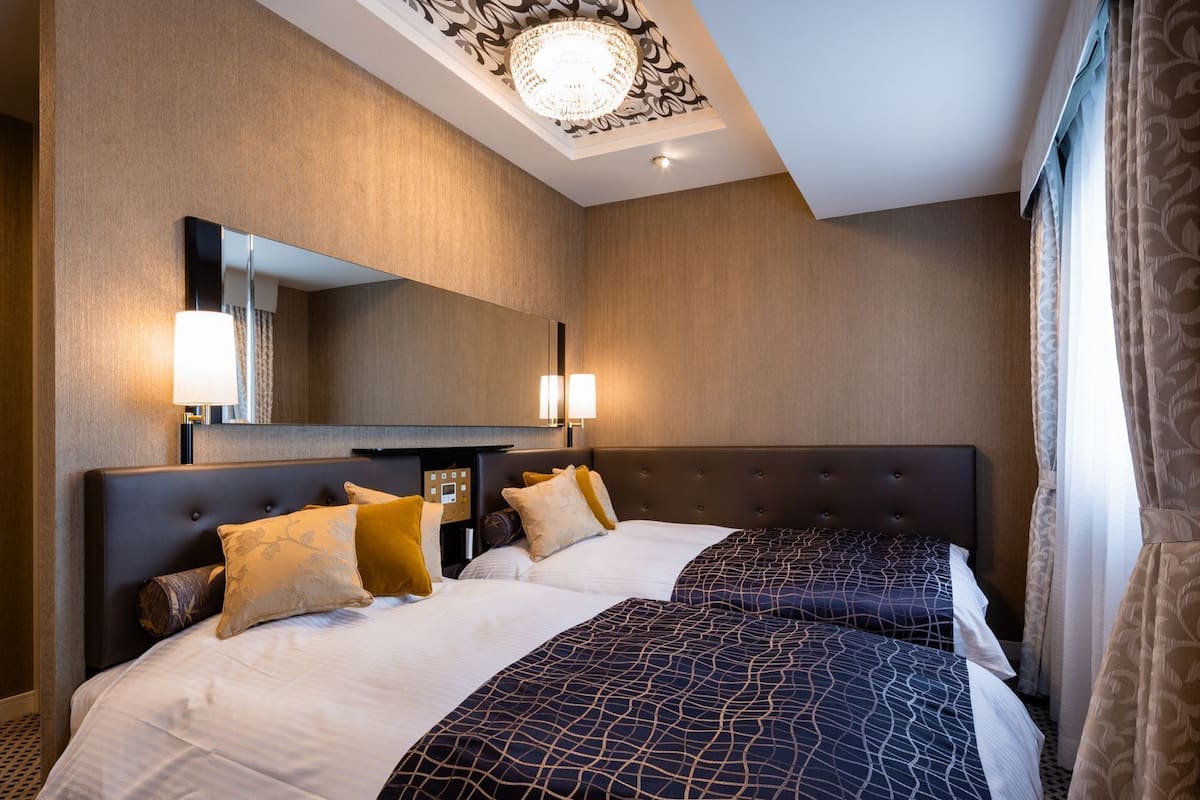 A hotel room with two beds, a large mirror, wall sconces, and a chandelier.