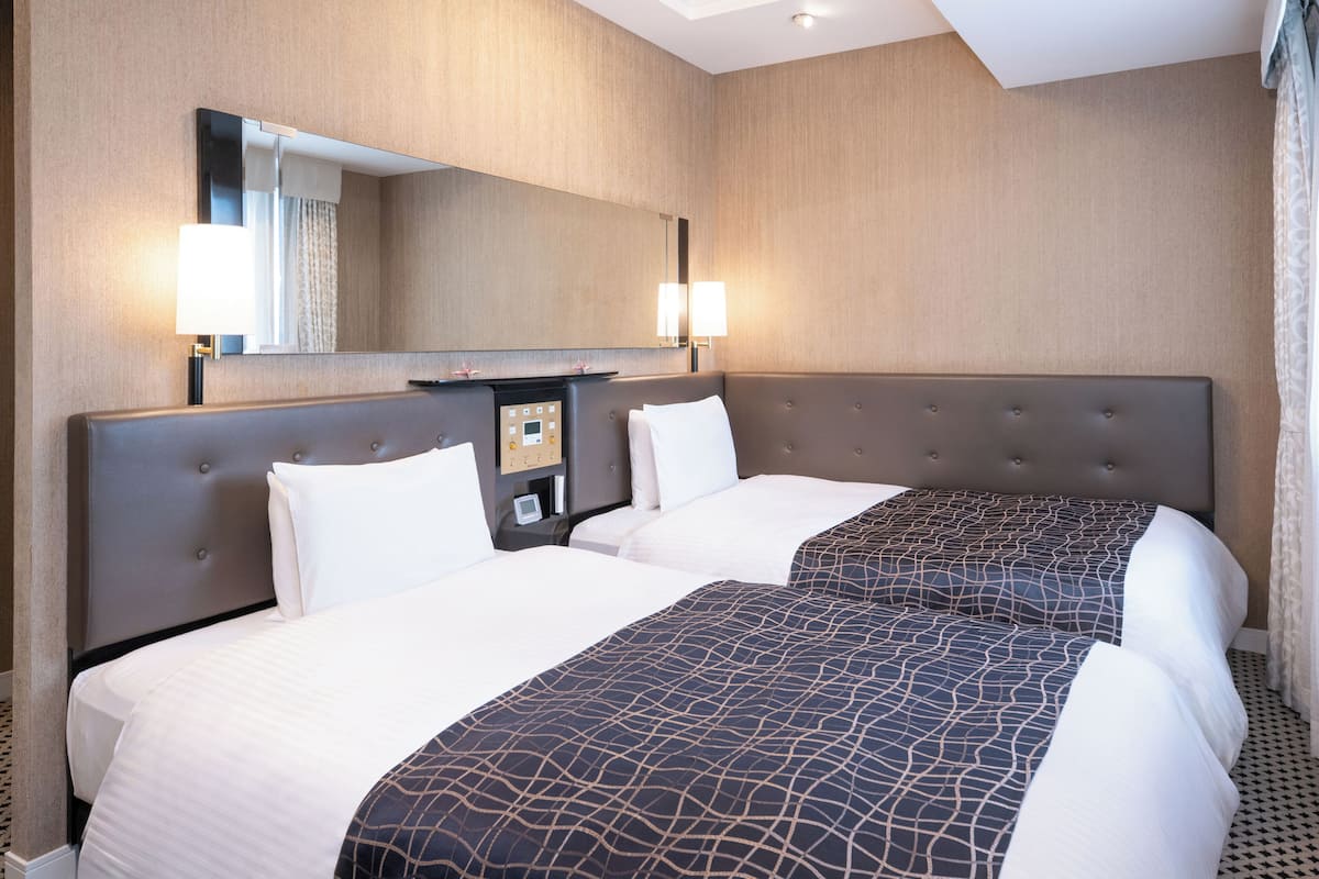 A hotel room with two beds, a large mirror, and a control panel on the wall.