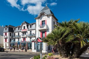 Ein mehrstöckiges Hotel mit Balkonen, einer rot-weißen Fassade und einer Palme im Vordergrund.