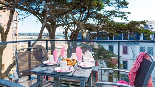 A balcony table set with plates, cups, and a teapot, overlooking a beach and buildings. - Apartment in La Baule with Sea View (PORNICHET)