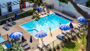 A swimming pool with lounge chairs and umbrellas, surrounded by a fenced area with a building in the background. - Apartment in La Baule with Sea View (PORNICHET)
