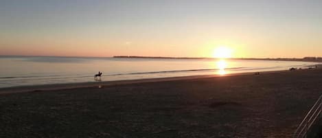 A beach at sunset with a horse and rider, calm sea, and distant shoreline.