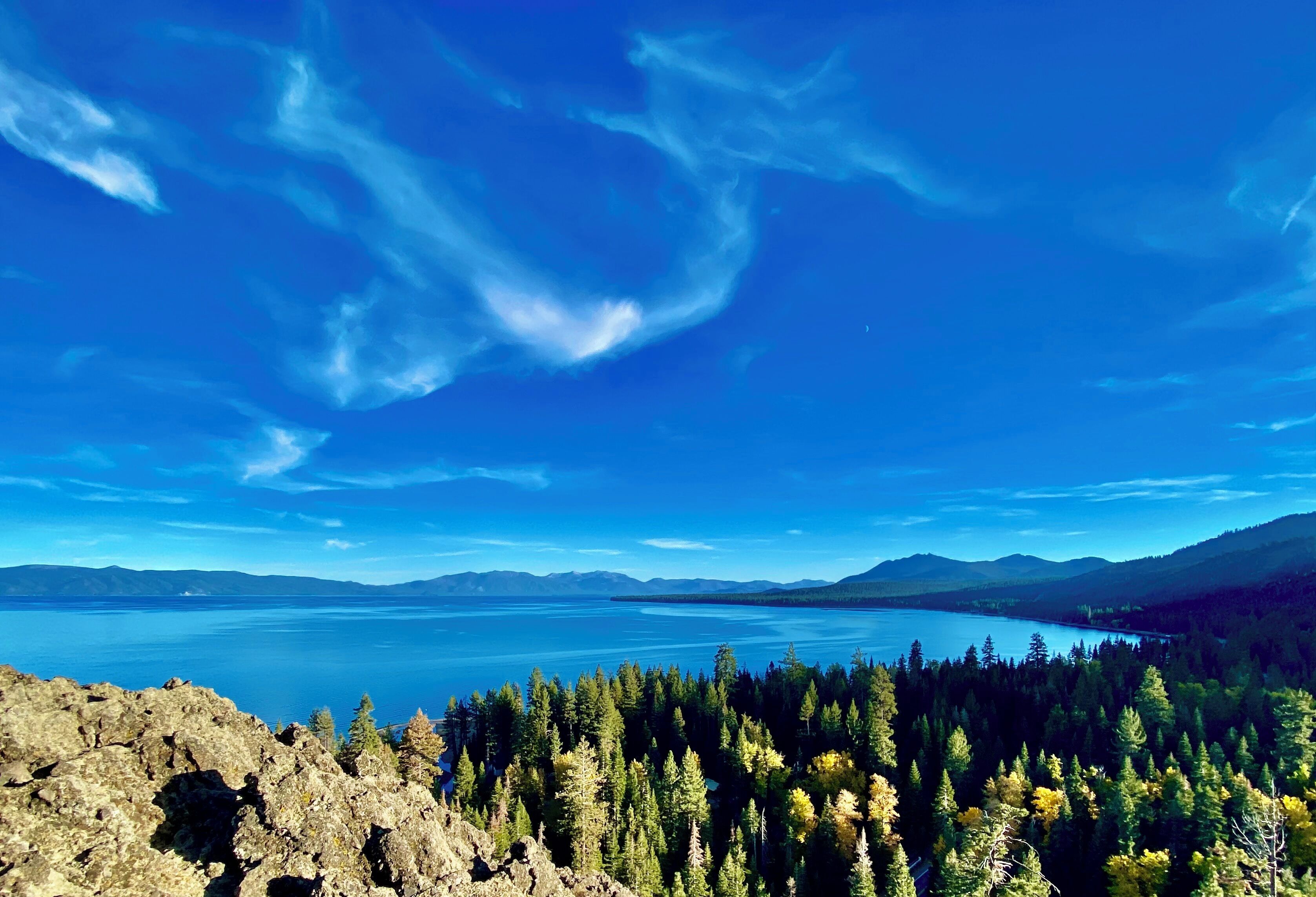A mountainous landscape with a clear blue sky, a lake, and dense forest.