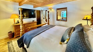Una camera da letto con soffitto in legno, un letto con coperta blu, una cassettiera, una TV e uno specchio.