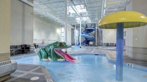 An indoor swimming pool with a large frog sculpture, a water slide, and a yellow dome structure.