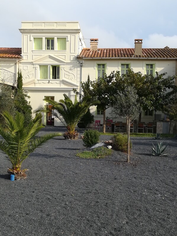 A building with a symmetrical facade, a gravel driveway, and a variety of plants.