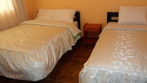 Two single beds with matching headboards and footboards, a wooden nightstand between them, and a window with curtains. - Hospedaje Imperio Inka (Cusco)