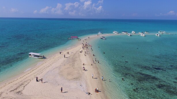 Una playa con aguas turquesas cristalinas, una orilla arenosa y varias embarcaciones fondeadas cerca.