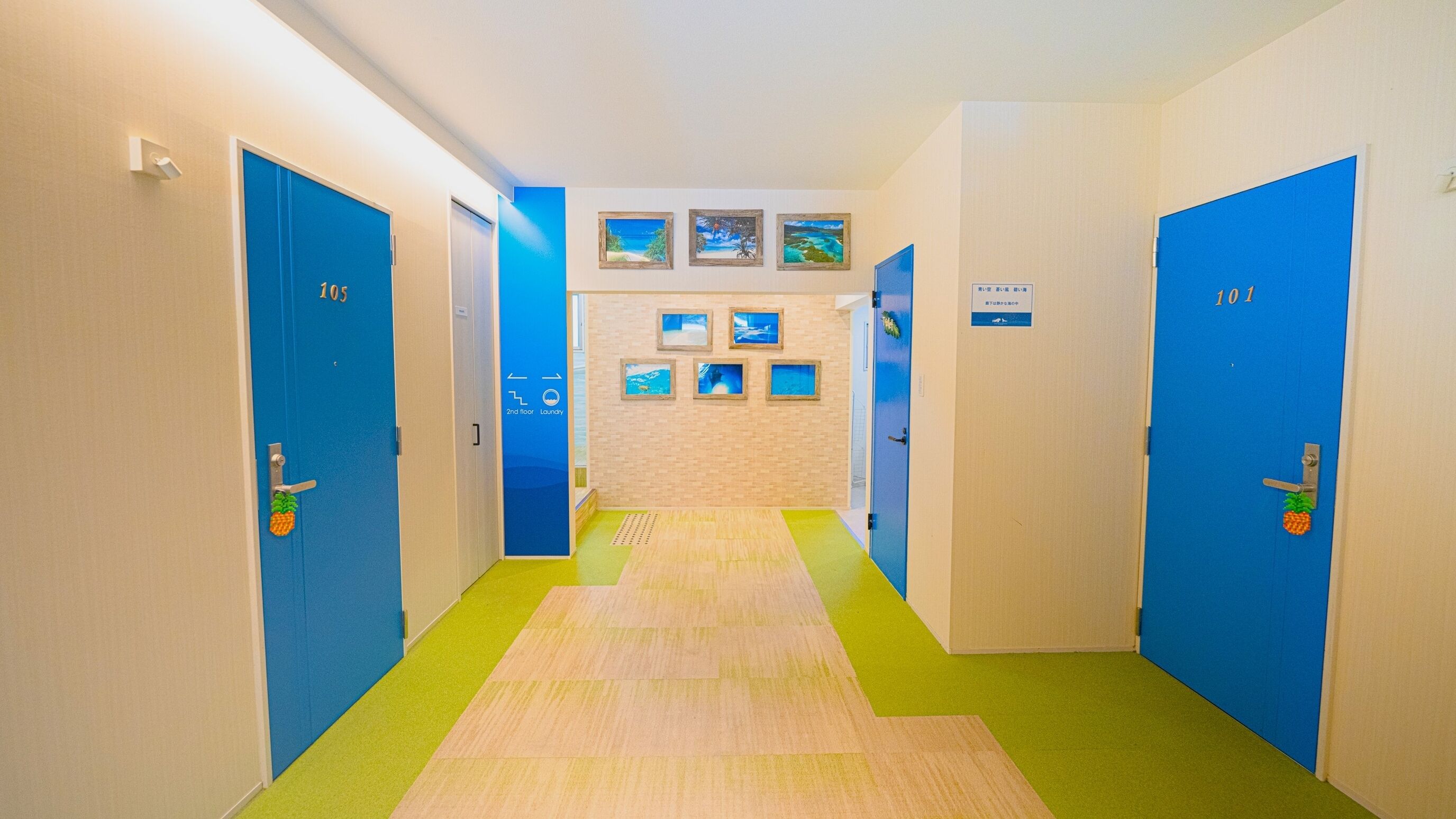 A hotel hallway with blue doors numbered 101 and 103, leading to a room with a beach-themed wall.
