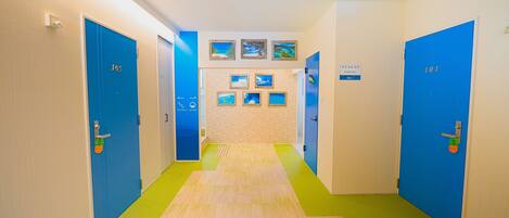 A hotel hallway with blue doors numbered 101 and 103, leading to a room with a beach-themed wall.
