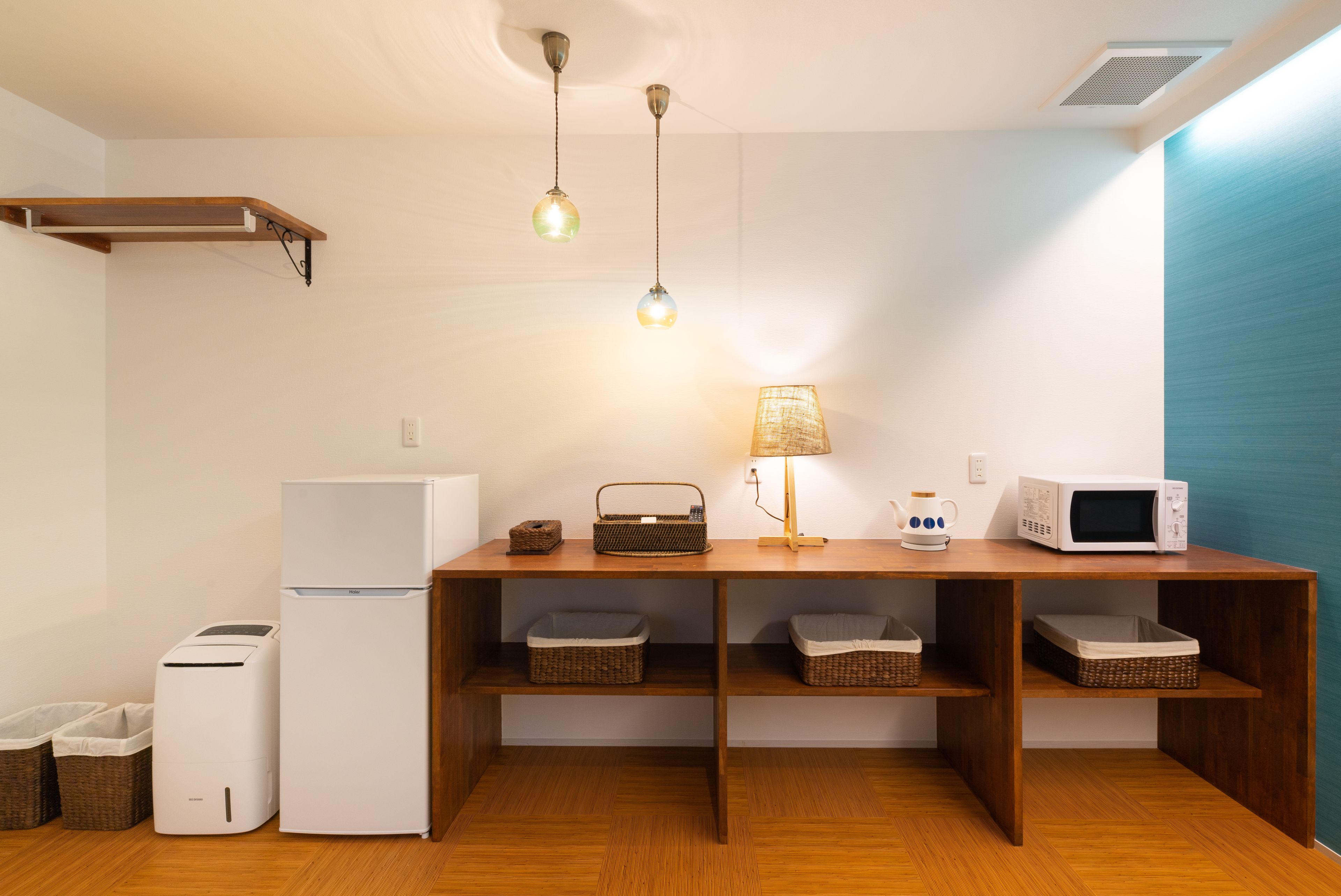 A compact kitchen with a refrigerator, microwave, toaster, and wicker baskets on shelves.