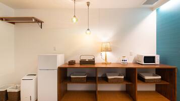 A compact kitchen with a refrigerator, microwave, toaster, and wicker baskets on shelves.