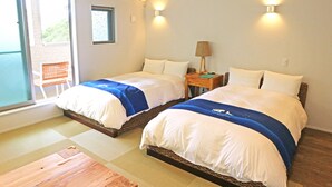 Habitación de hotel con dos camas, una puerta corrediza de vidrio al balcón y una mesita de noche con lámpara.