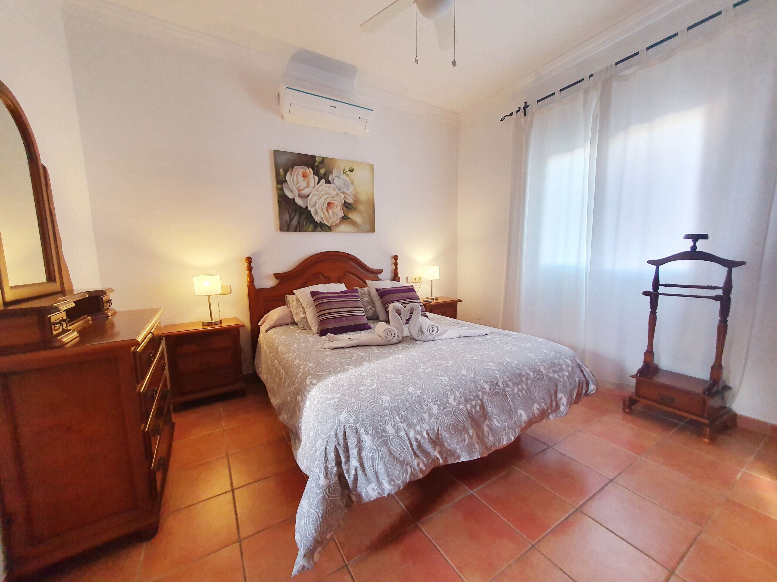 A neatly arranged bedroom with a bed, bedside tables, a mirror, and a wooden chair.