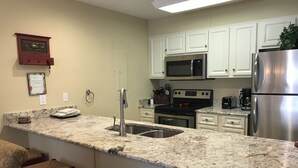 A kitchen with white cabinets, a stainless steel refrigerator, a microwave, and a stove. There is a granite countertop and a sink with a faucet.