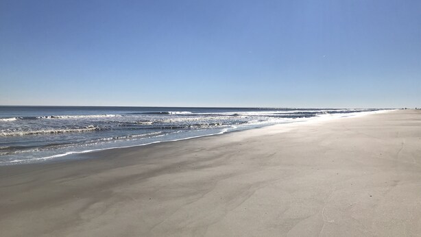A wide sandy beach with gentle waves and a clear blue sky.