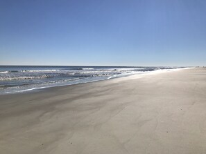 A wide sandy beach with gentle waves and a clear blue sky.