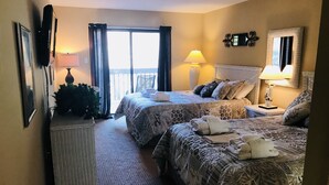 A hotel room with two beds, a small table, a chair, a balcony, and a large window.