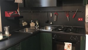 A kitchen with dark green cabinets, a stainless steel sink, a stove, and a hanging rack with kitchen utensils. - Apartment in the historic center (Ferrara)