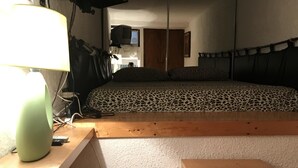 A bedroom with a bed, a desk with a lamp, a TV, and a small wooden stool. - Apartment in the historic center (Ferrara)
