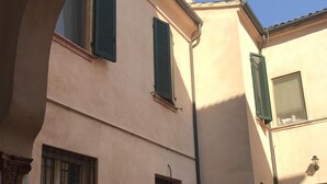A building with a beige facade, green shutters, and a barred window. There is a bicycle in the foreground and potted plants around. - Apartment in the historic center (Ferrara)