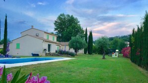 Une maison avec une piscine, entourée d’une pelouse bien entretenue et de divers arbres.