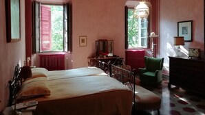 A room with a bed, a green armchair, a dresser, and a desk with a lamp.